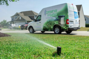 A Conserva Irrigation franchise service van parked on a street, with a sprinkler system actively watering the lush green lawn in the foreground.